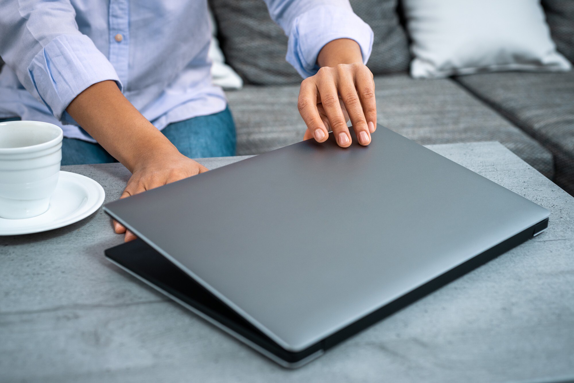Widok dłoni kobiety otwierającej pokrywę laptopa. W pobliżu jest biała filiżanka kawy.