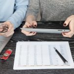 Środkowa sekcja kolegów używających cyfrowego tabletu za pomocą laptopa i raportu na biurku