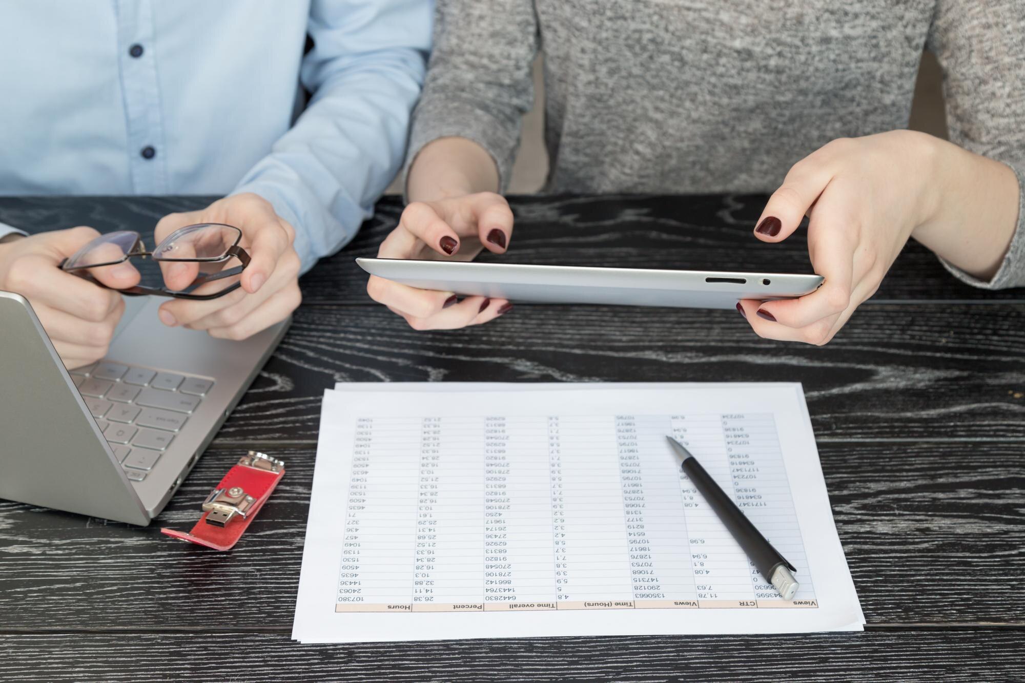 Środkowa sekcja kolegów używających cyfrowego tabletu za pomocą laptopa i raportu na biurku