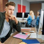 Przemyślany informatyk siedzi przy stole w biurze. Programista lub projektant sieci w miejscu pracy, zawód twórczy. Nowoczesna technologia informacyjna, zespół korporacyjny