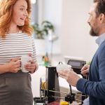 Pozytywnie sympatyczni zachwyceni koledzy rozmawiają ze sobą i piją kawę w pracy