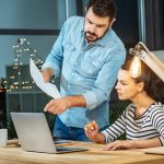 Pracować razem. Przystojny inteligentny miły mężczyzna stojący obok swojego kolegi i wskazując na ekran laptopa podczas współpracy z nią