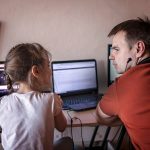 Ojciec w średnim wieku pracujący online blisko swojej uroczej córki podczas jej zajęć online w domu