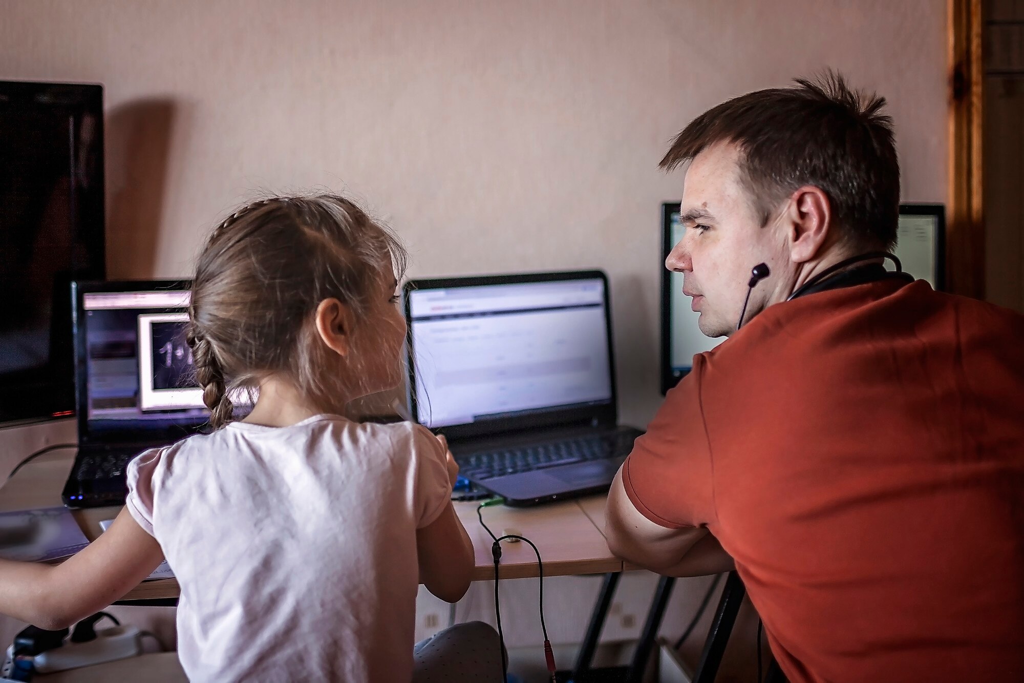 Ojciec w średnim wieku pracujący online blisko swojej uroczej córki podczas jej zajęć online w domu