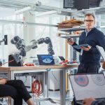 Główny inżynier trzyma tablet i rozmawia z różnorodnym zespołem specjalistów w dziedzinie informatyki o komponentach płyty głównej na zamkniętej konferencji Zainspirował ludzi do opracowania programów dla futurystycznego ramienia robotycznego