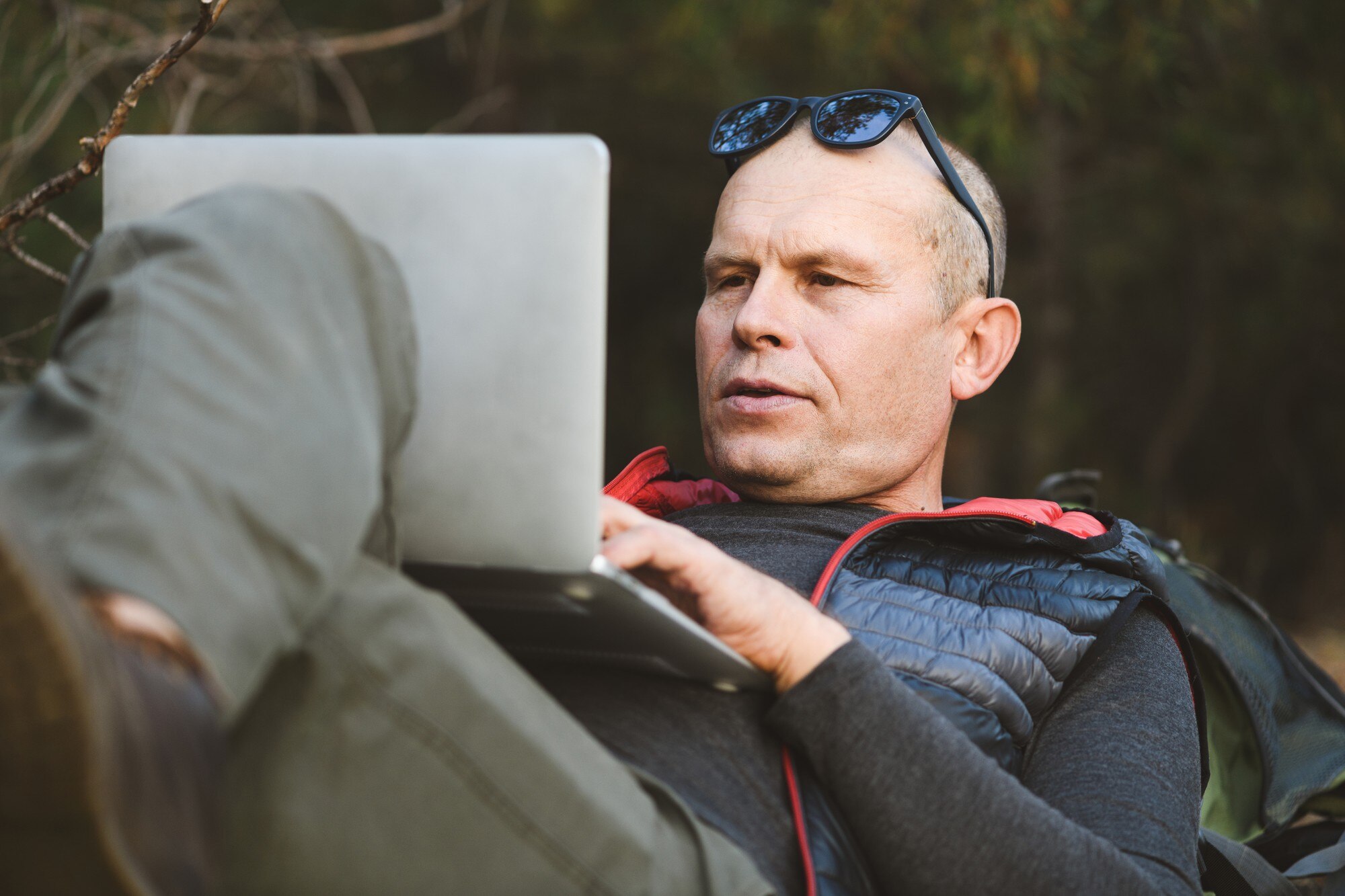 Zbliżenie: mężczyzna turysta leżący na plecach, opierając się na plecaku, z laptopem, pisanie na maszynie, blogowanie, przeglądanie w lesie
