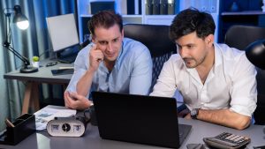 Partnerzy biznesowi skupiający się na laptopie pracujący razem z dobrym stosunkiem w nocy w nowoczesnym biurze analizując kreatywny projekt w niebieskim neonowym pokoju dekoracyjnym Koncepcja burzy mózgów Sprzedawalna