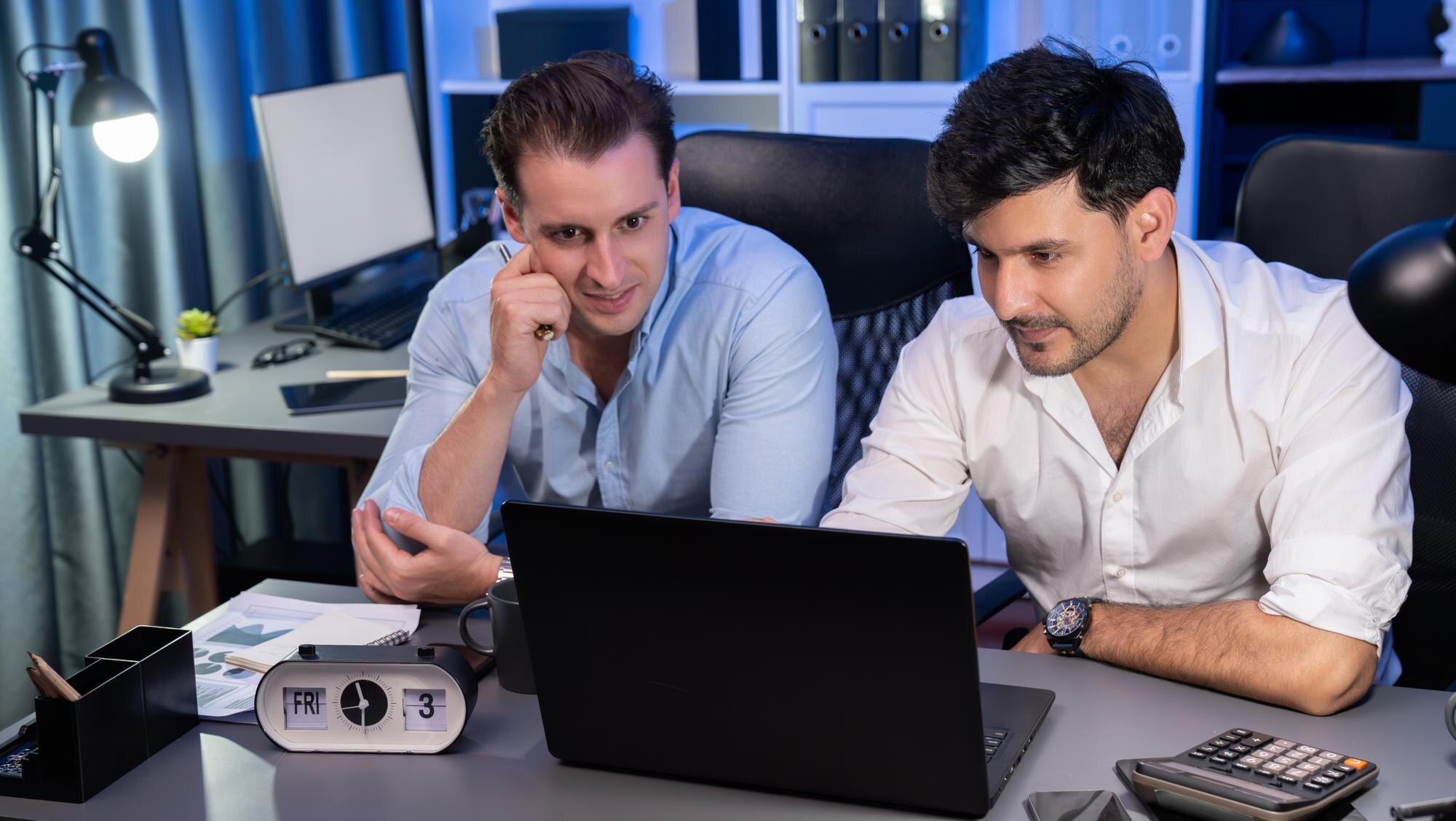 Partnerzy biznesowi skupiający się na laptopie pracujący razem z dobrym stosunkiem w nocy w nowoczesnym biurze analizując kreatywny projekt w niebieskim neonowym pokoju dekoracyjnym Koncepcja burzy mózgów Sprzedawalna