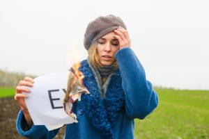 Smutna dziewczyna trzyma płonący papier z ogniem i wydrukowanym napisem Ex o chłopaku, mężu, zerwanych związkach, rytuale rozwodu