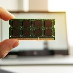 Ręka z pamięcią na płycie głównej komputera. RAM w ręku na tle laptopa.