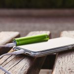 Smartfon i zewnętrzny power bank leżą na drewnianej ławce w parku podczas ładowania