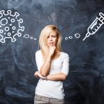 Ładna młoda blondynka dokonuje wyboru między szczepieniem koronawirusa na tle ciemnej tablicy kredowej. Koncepcja szczepień i wirusów. COVID-19. Pandemia. Kobieta myśli o koronawirusie