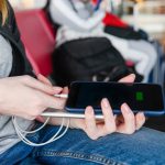 Kobieta podróżująca podłącza baterię telefonu komórkowego do przenośnej ładowarki w poczekalni na lotnisku za pomocą kabla USB z bliska