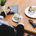 Kobieta pije kawę w kawiarni na ulicy. Zbliżenie: tabletka, szklanki, kawa i deser na drewnianym stole.