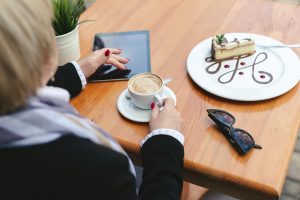 Kobieta pije kawę w kawiarni na ulicy. Zbliżenie: tabletka, szklanki, kawa i deser na drewnianym stole.