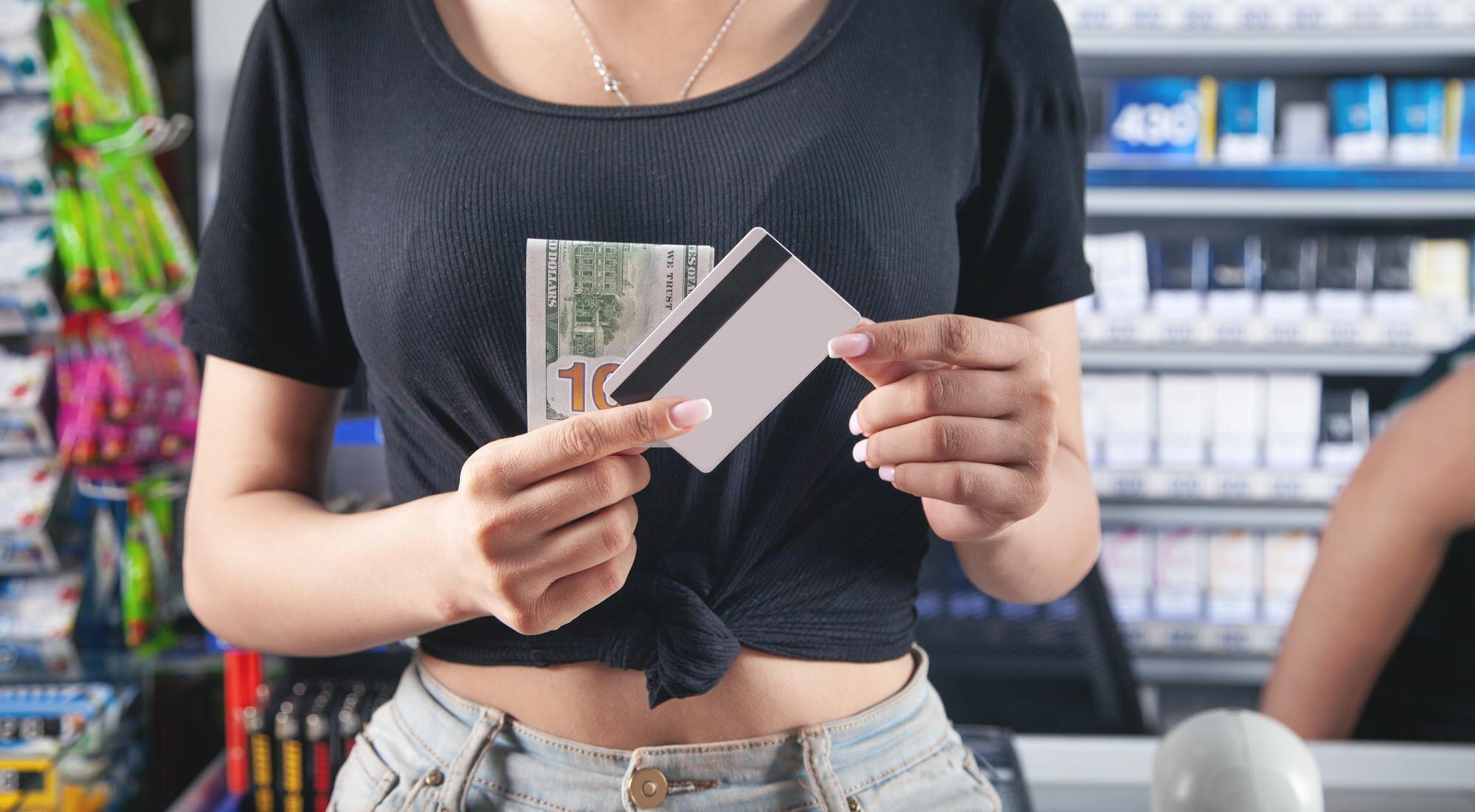 Kobieta trzyma kartę kredytową i pieniądze w supermarkecie.