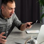 Mad zestresowany młody człowiek zły z powodu awarii laptopa lub komputera, wściekły facet zirytowany wirusem powodującym problemy z komputerem, użytkownik zdezorientowany fałszywymi złymi wiadomościami online, sfrustrowany awarią notebooka lub utratą danych.