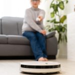 koncepcja ludzie, rozrywka, gospodarstwo domowe i technologia - starsza kobieta, robot odkurzający podłogę w domu.