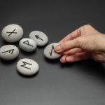 Wróżenie z symbolami na kamieniu Dłoń trzymająca nordyckie kamienie runiczne z czarnymi symbolami