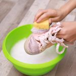 Kobieta myjąca tenisówki z gąbką nad zbliżeniem plastikowej umywalki