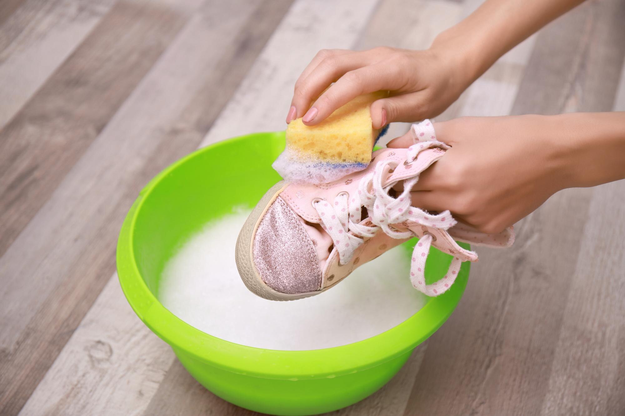 Kobieta myjąca tenisówki z gąbką nad zbliżeniem plastikowej umywalki