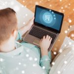 koncepcja technologii, wypoczynku, reklamy i stylu życia - zbliżenie człowieka pracującego z laptopem wyświetlającego ikonę wózka na zakupy na ekranie i siedzącego na kanapie w domu