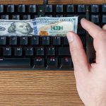 ręka próbuje złapać dolary leżące na czarnej klawiaturze