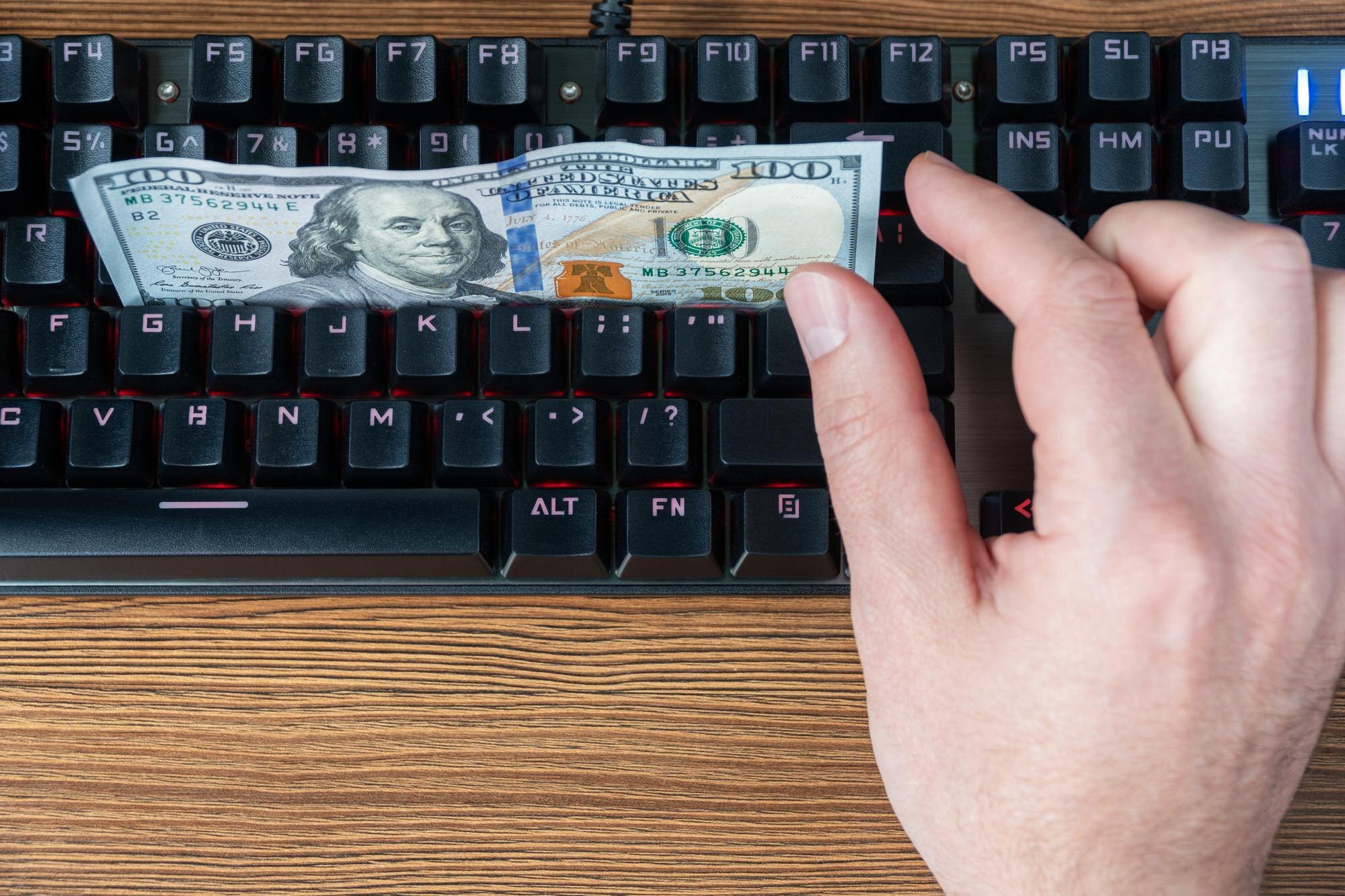 ręka próbuje złapać dolary leżące na czarnej klawiaturze