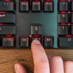 męski palec ręki naciska strzałkę w dół na klawiaturze leżącej na drewnianym stole, zbliżenie