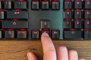 męski palec ręki naciska strzałkę w dół na klawiaturze leżącej na drewnianym stole, zbliżenie