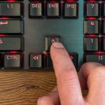 palec ręki mężczyzny naciska strzałkę w górę na klawiaturze leżącej na drewnianym stole, zbliżenie