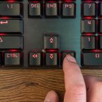 męski palec ręki naciska strzałkę w prawo na klawiaturze leżącej na drewnianym stole, zbliżenie