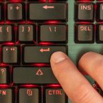 Mężczyzna naciska klawisz Enter na czarnej klawiaturze z czerwonym podświetleniem