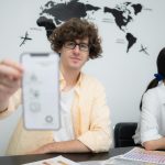 Wieloetniczny zespół architektów i projektantów spotyka się, aby zaprojektować aplikację dla smartfonów w jasnym nowoczesnym biurze pracującym na laptopie