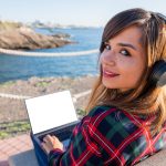 Dziewczyna używa swojego laptopa nad morzem, siedząc na ekranie ławki z makietą