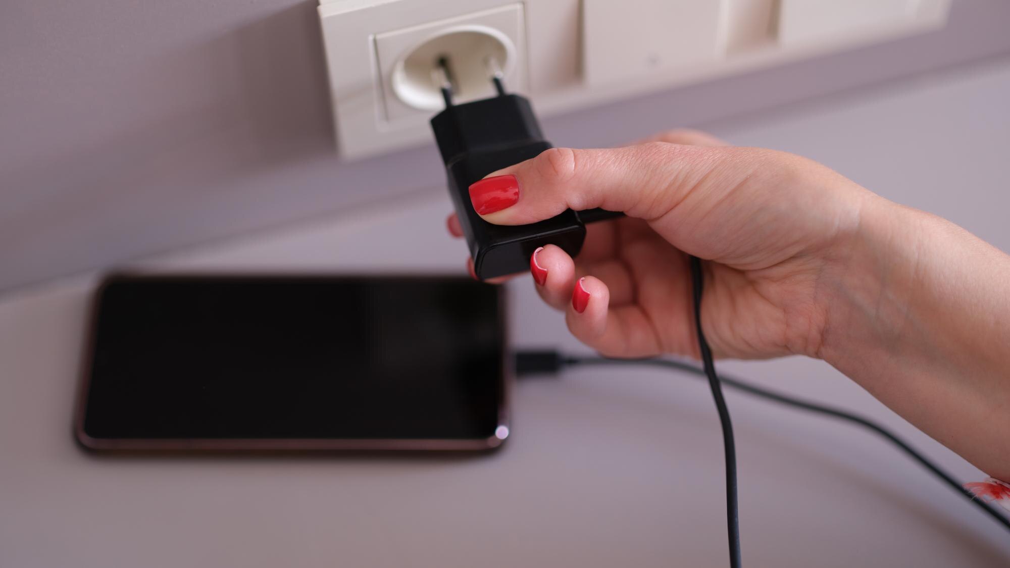 Kobieta z ładowarką do telefonu komórkowego w nasadce na ścianie