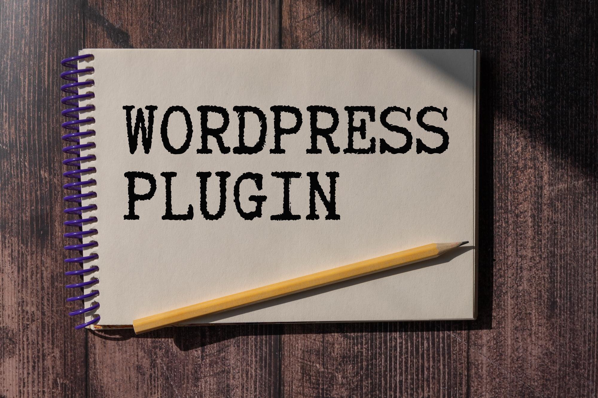 Notatnik z tekstem WORDPRESS PLUGIN długopis i okulary leżą na drewnianym biurowym stole