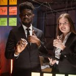 Ludzie w strojach formalnych, używający samoprzylepnych notatek i piszący, stojąc za szklaną ścianą