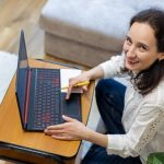 Uśmiechnięta kobieta pracująca na laptopie w domu szczęśliwa kobieta siedząca na kanapie używająca laptopa trzymającego długopis i