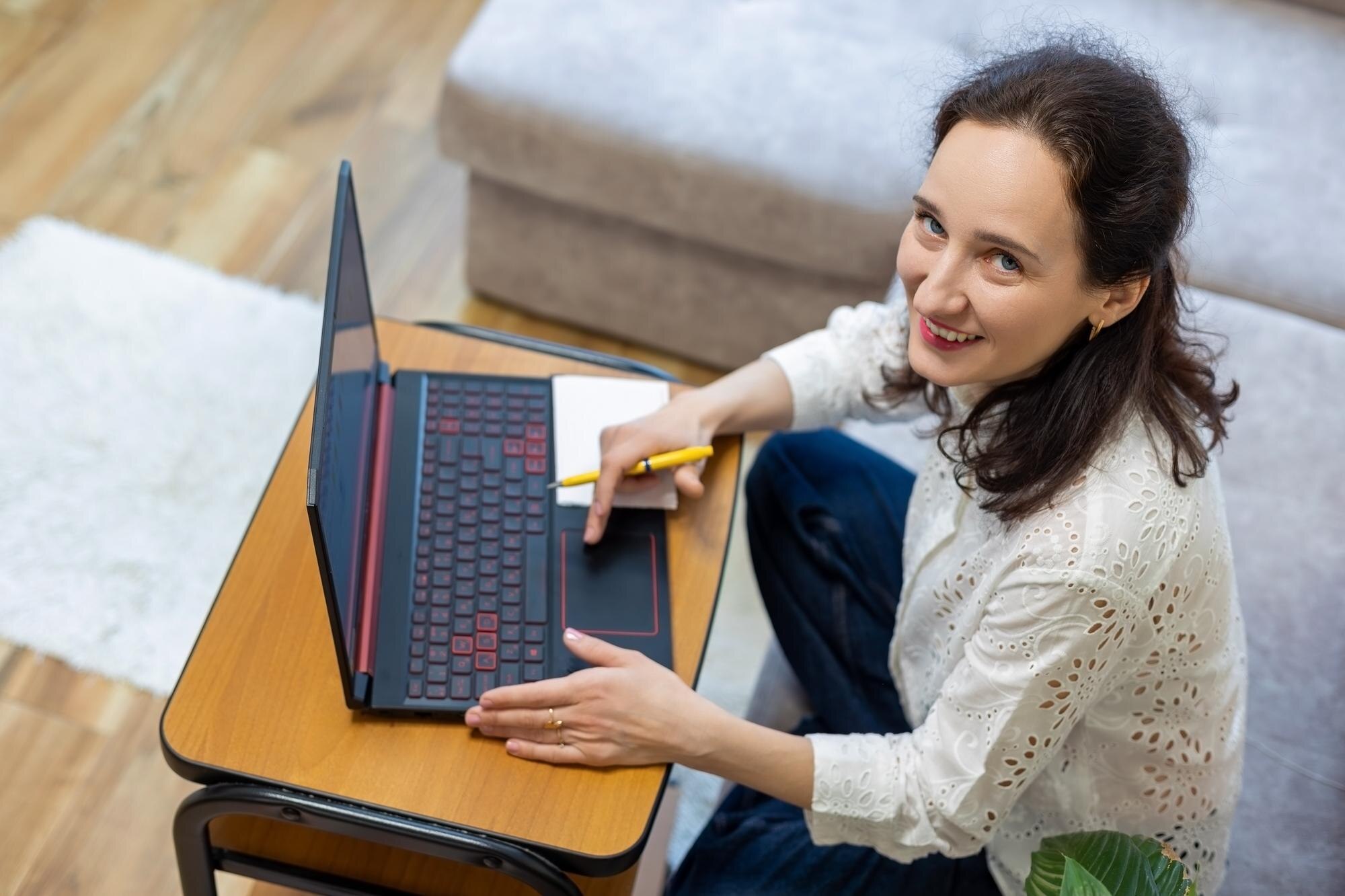 Uśmiechnięta kobieta pracująca na laptopie w domu szczęśliwa kobieta siedząca na kanapie używająca laptopa trzymającego długopis i