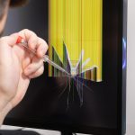 Skilled technician assessing a severely cracked computer monitor screen with a screwdriver symbolizing urgent technology repair service and common hardware malfunction issues