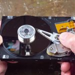 Hands holding an open hard disk drive revealing internal components