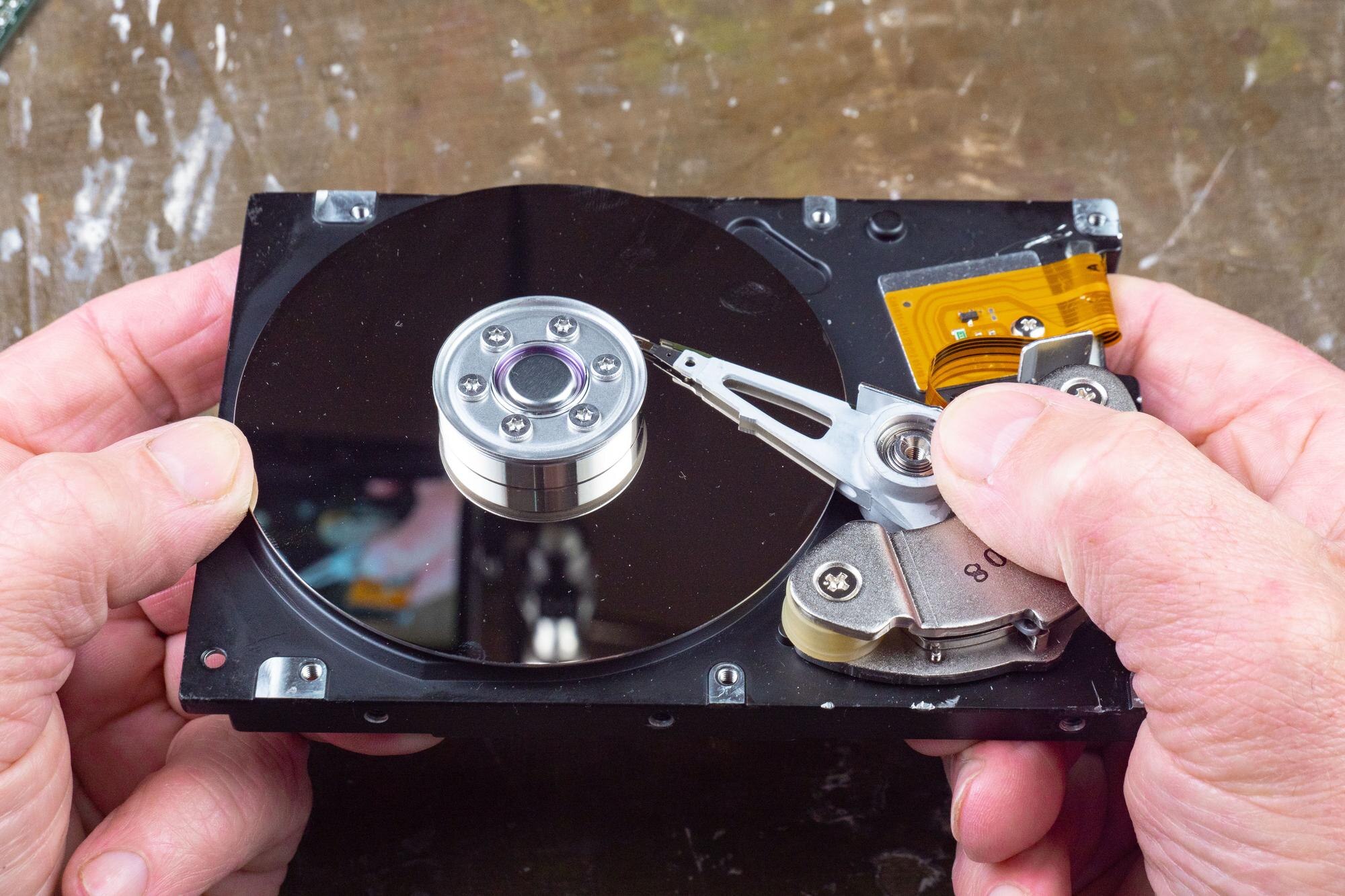 Hands holding an open hard disk drive revealing internal components