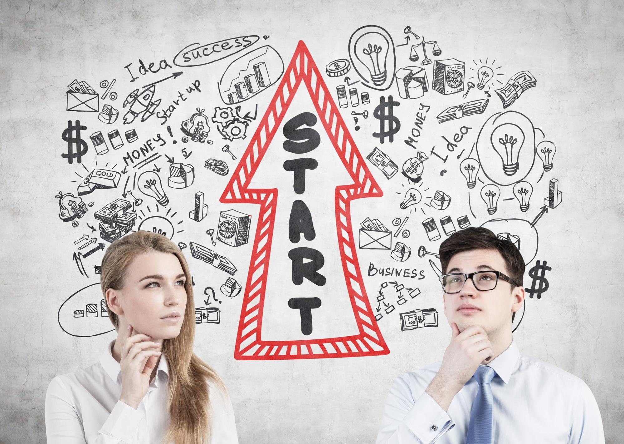 Portret biznesmena w okularach i jego blond kolega stojący przy betonowej ścianie z narysowanym na nim szkicem startowym.