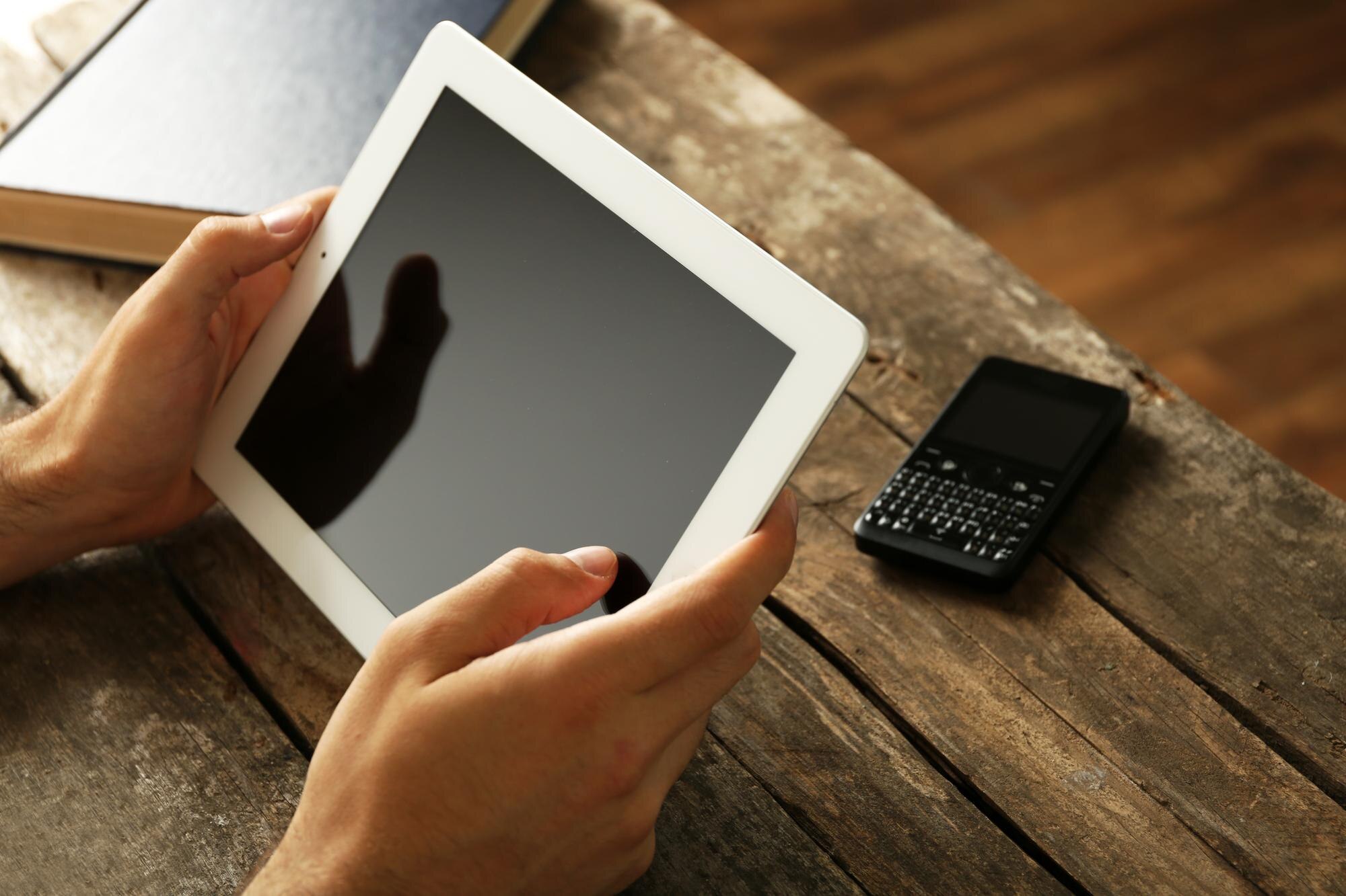 Ręce trzymające cyfrowy tablet na drewnianym tle stołu