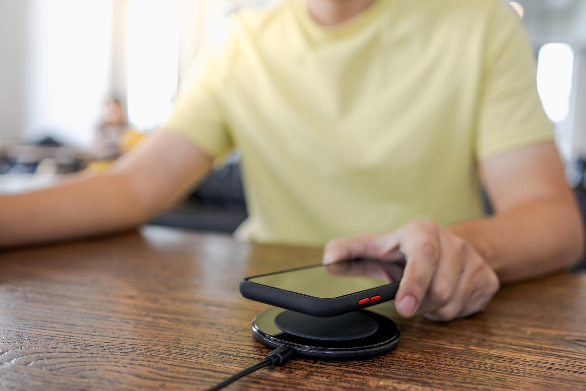 Ładowanie baterii telefonu komórkowego za pomocą urządzenia bezprzewodowego w stole Ładowanie smartfonu na poduszce ładującej Telefon komórkowy w pobliżu ładowarki bezprzewodowej