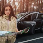 Młoda kobieta samotnie podróżujący samochodem z mapą. Koncepcja jesień. Jesienna leśna podróż samochodem.