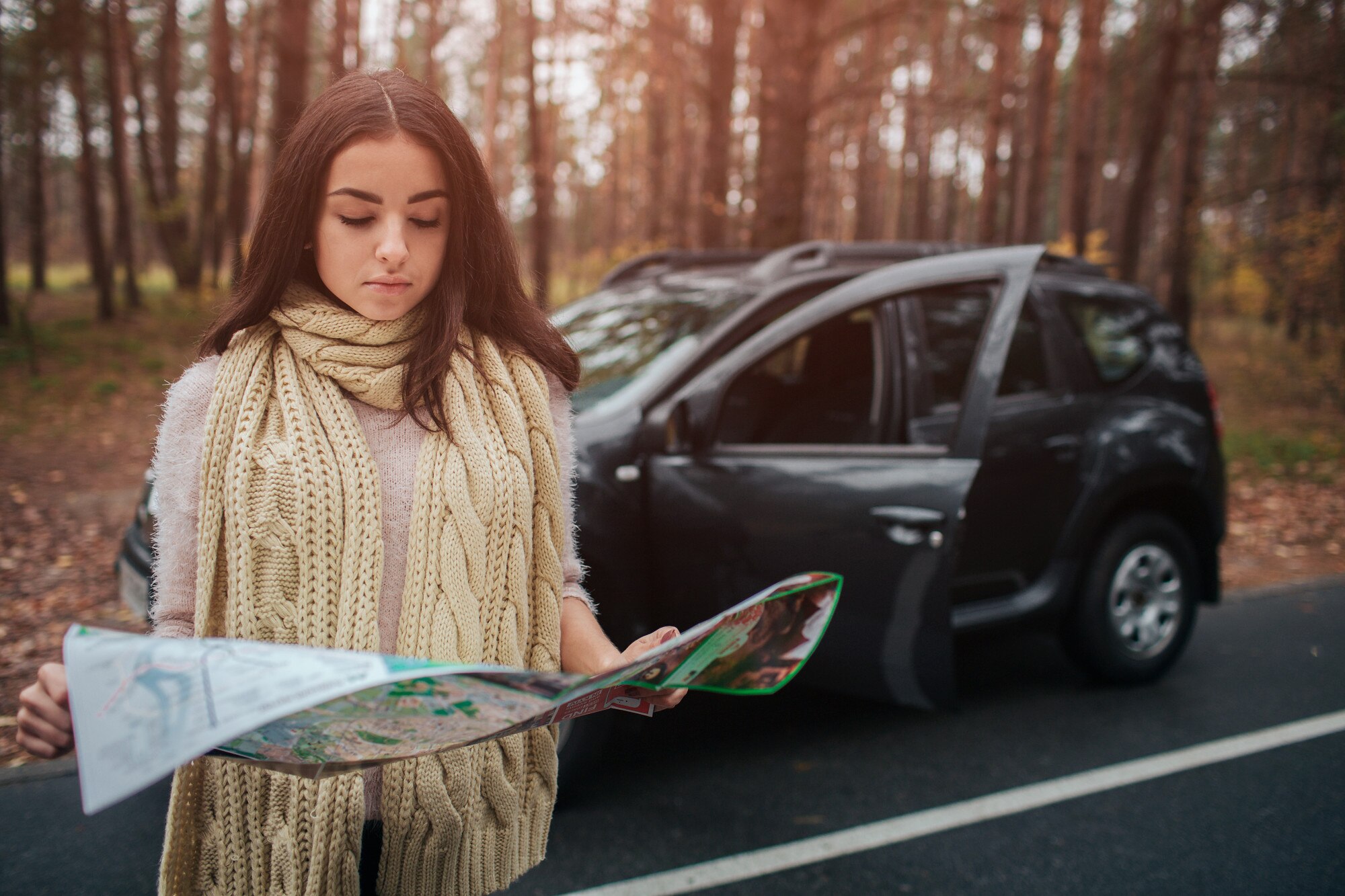 Młoda kobieta samotnie podróżujący samochodem z mapą. Koncepcja jesień. Jesienna leśna podróż samochodem.