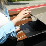 Dziewczyna pracuje na laptopie, siedząc na ławce